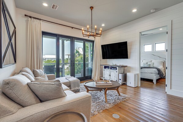 A modern living room with a sofa, a coffee table, and a TV. - Luxe Beachfront Windmark Cottage w/ Deck! (Port St. Joe)