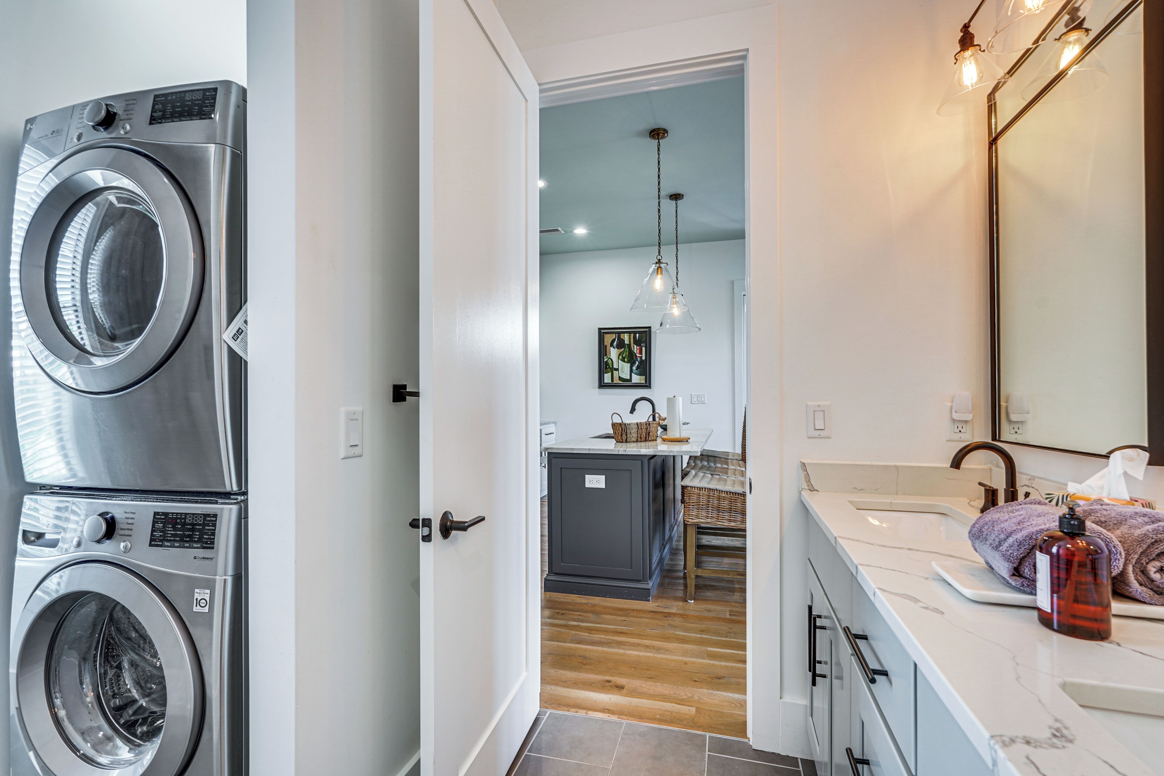 A laundry room with stacked washers and dryers, a kitchen area with a dining table, and a bathroom with a large mirror and towel rack.