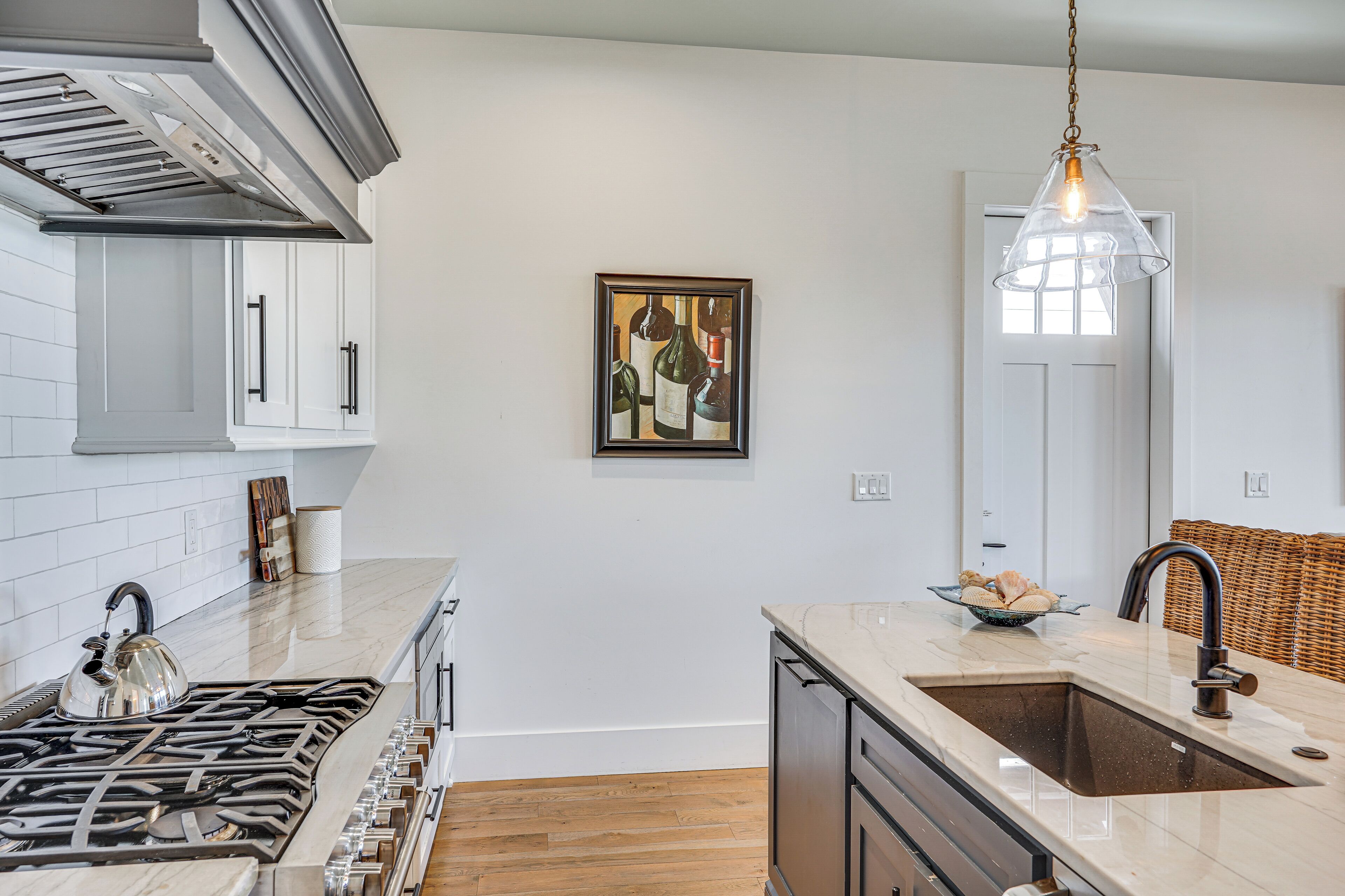 A modern kitchen with white cabinetry, a stainless steel range hood, a large island with a sink, and a hanging pendant light.