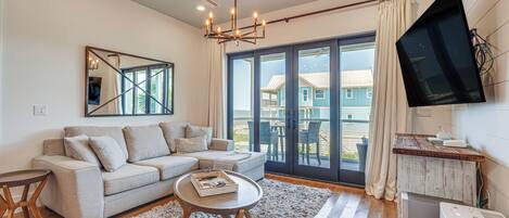 A modern living room with a grey sofa, a round coffee table, and a large window with a view of a blue house.