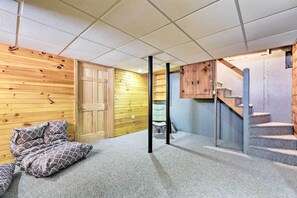A room with a wooden wall, a door, a staircase, and a bed with patterned bedding. - Oceanfront Cape Cod Home w/ Porch, Yard + Grill! (Marshfield)