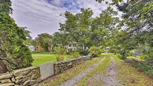 A stone wall with a wooden fence, a gravel path, and houses in the background. - Mattapoisett Home on 7 Acres w/ Private Beach! (Mattapoisett)
