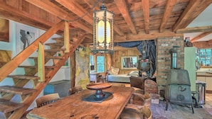A rustic wooden interior with a large wooden table, a wooden staircase, and a brick fireplace. - Serene Riverfront Stay! 'the Mill River Cabin (Mill River)