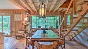 A rustic wooden interior with a dining table, chairs, and a staircase. - Serene Riverfront Stay! 'the Mill River Cabin (Mill River)
