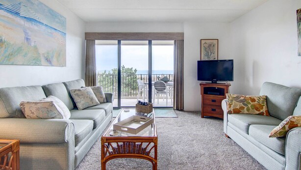 Un salon avec un canapé, une table basse, un téléviseur et un balcon offrant une vue agréable.