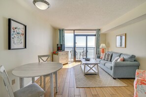 A living room with a grey sofa, a round dining table, and a TV. - 1 Mi to Myrtle Beach Boardwalk: Oceanfront Condo (Myrtle Beach)
