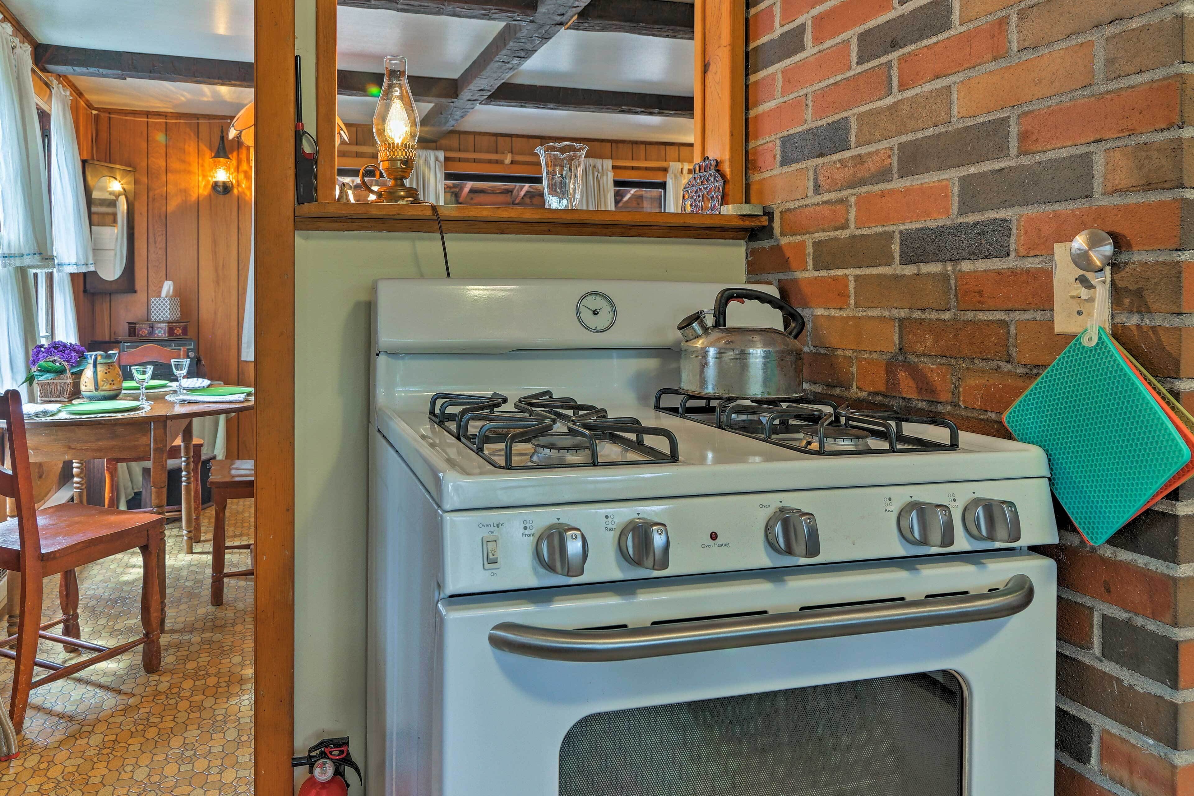 A kitchen with a white stove, wooden chairs, a dining table, and a brick wall.