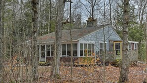 A rustic cabin surrounded by trees, with a chimney and a door with a yellow frame. - East Otis Reservoir Cabin w/ Porch - Walk to Lake! (Otis)