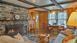 A cozy living room with a stone fireplace, wooden furniture, and a dining area with a table and chairs. - East Otis Reservoir Cabin w/ Porch - Walk to Lake! (Otis)
