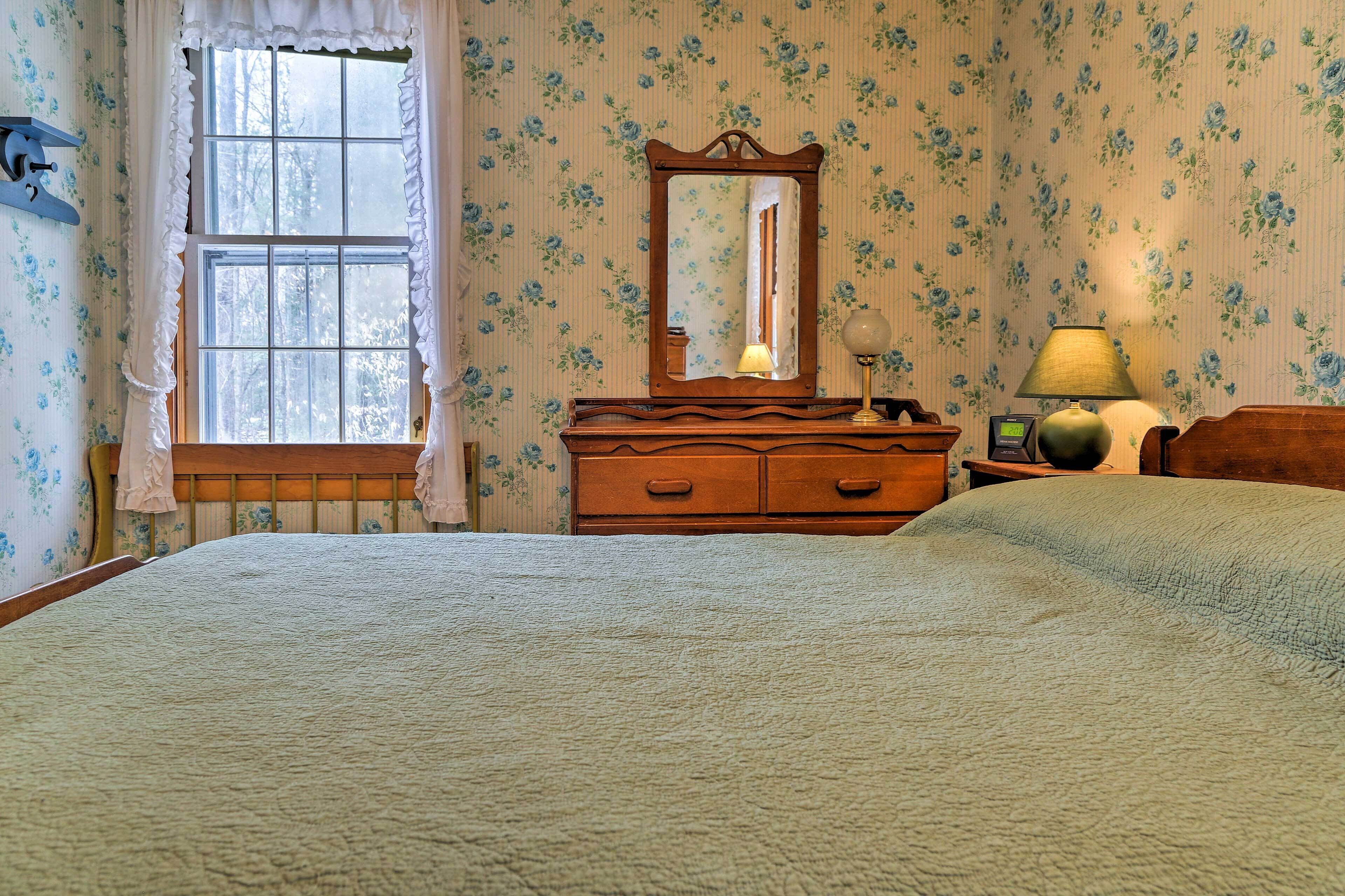 Une chambre à coucher avec un grand lit, une commode à tiroirs, un miroir, une lampe et une fenêtre avec des rideaux.