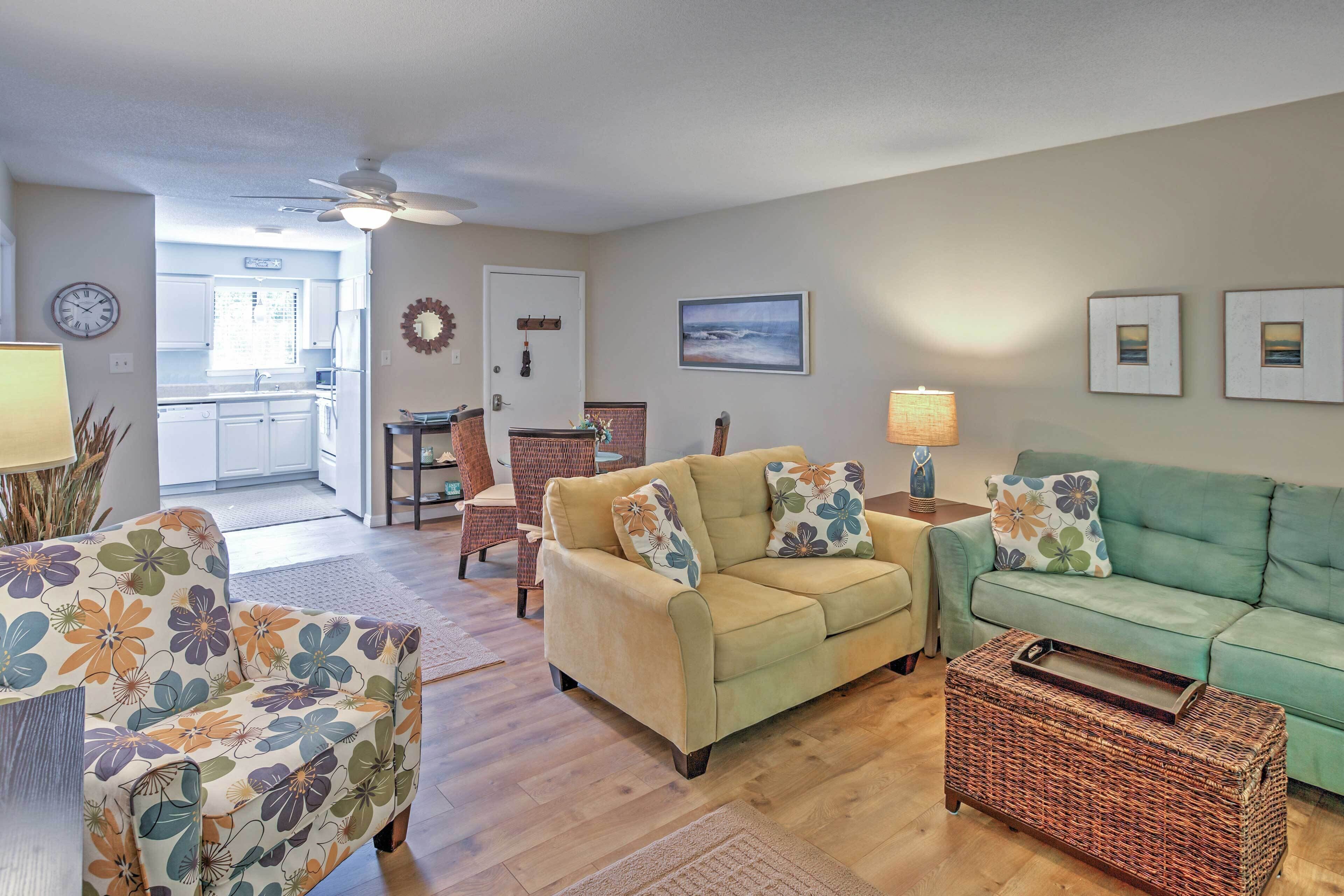 A living room with a beige sofa, a green sofa, and a floral armchair. There is a wicker side table with a tray.