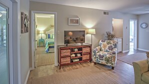 A living room with a TV, a floral armchair, and a wooden cabinet with baskets. - Amelia Island Condo w/ Pool & Beach Access! (Fernandina Beach)