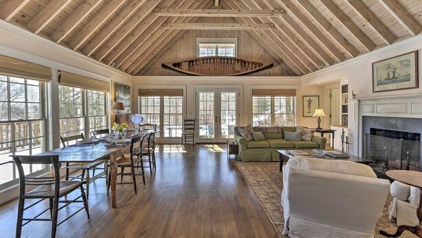 A spacious living area with a high ceiling, wooden beams, large windows, and a fireplace. - Waterfront Ipswich Escape: 2 Miles to Crane Beach! (Ipswich)