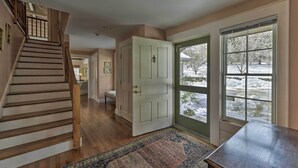 A staircase leading to a landing with a wooden railing, a white door, and a view of a snowy landscape through a glass door. - Waterfront Ipswich Escape: 2 Miles to Crane Beach! (Ipswich)