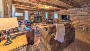 Un accogliente interno di una baita in legno con camino, divani in pelle, televisore e soffitto in legno.
