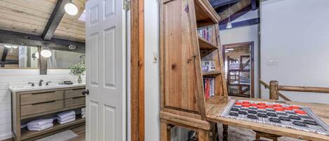 A room with a wooden cabinet, a table with a board game, and a bathroom with a sink and towels.