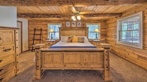 Camera da letto in una baita di legno con un letto grande, due comodini, una ventola a soffitto e due finestre con persiane.