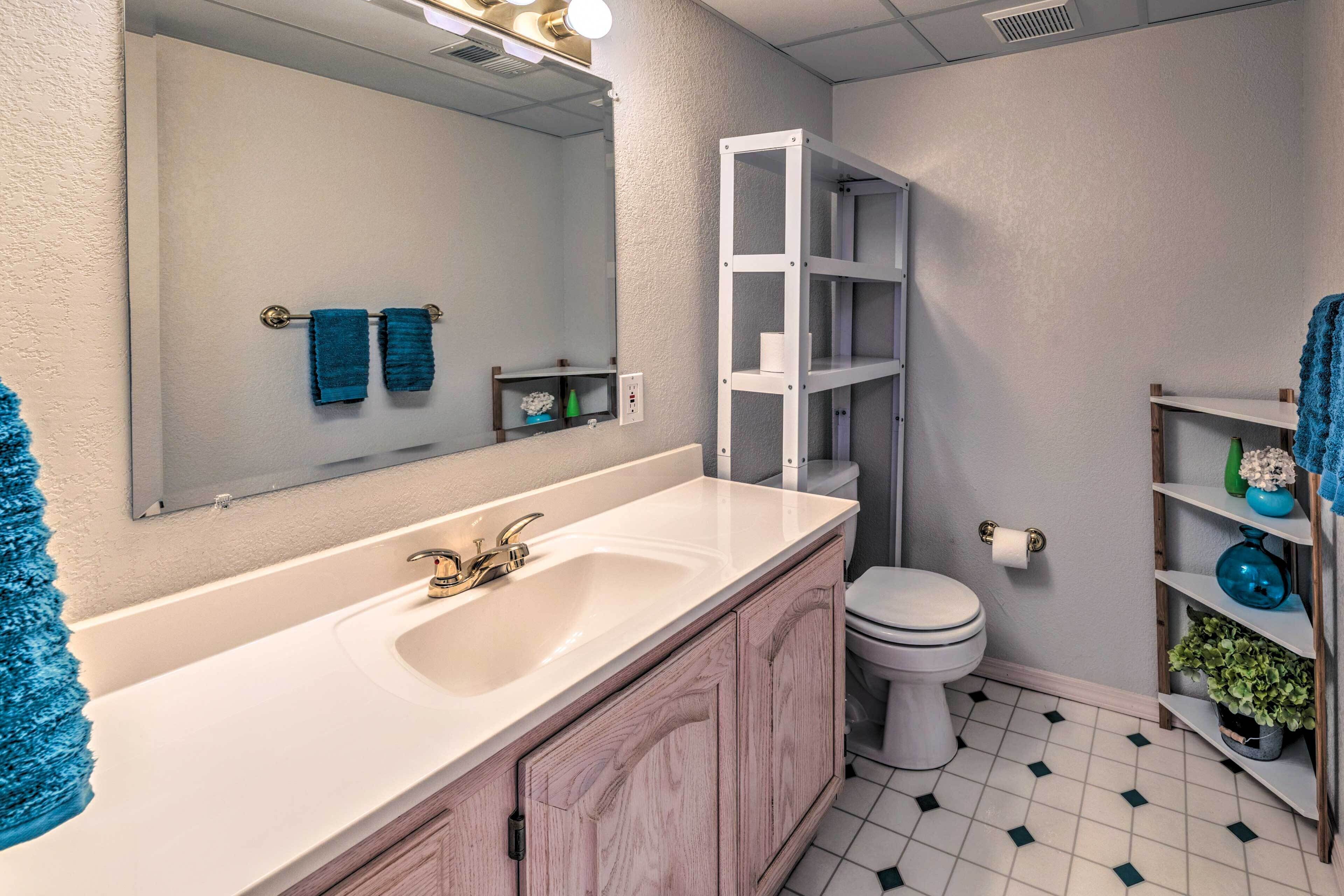 A bathroom with a white sink, a toilet, a mirror, and a shelf with toiletries.