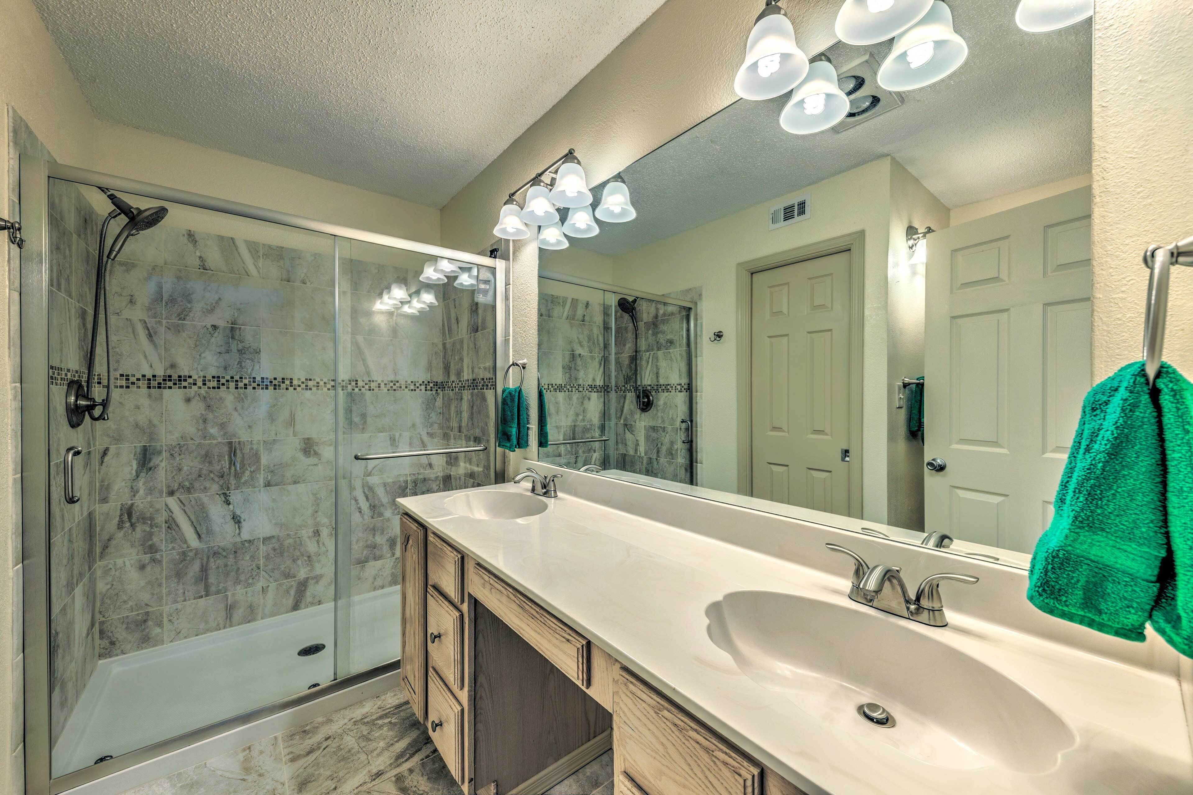 Une salle de bain dotée d’une douche à parois de verre, d’un grand miroir et d’un lavabo double avec un meuble-vasque en bois.