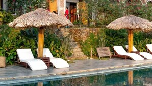 Zona de piscina con sillas de descanso y sombrillas de paja.