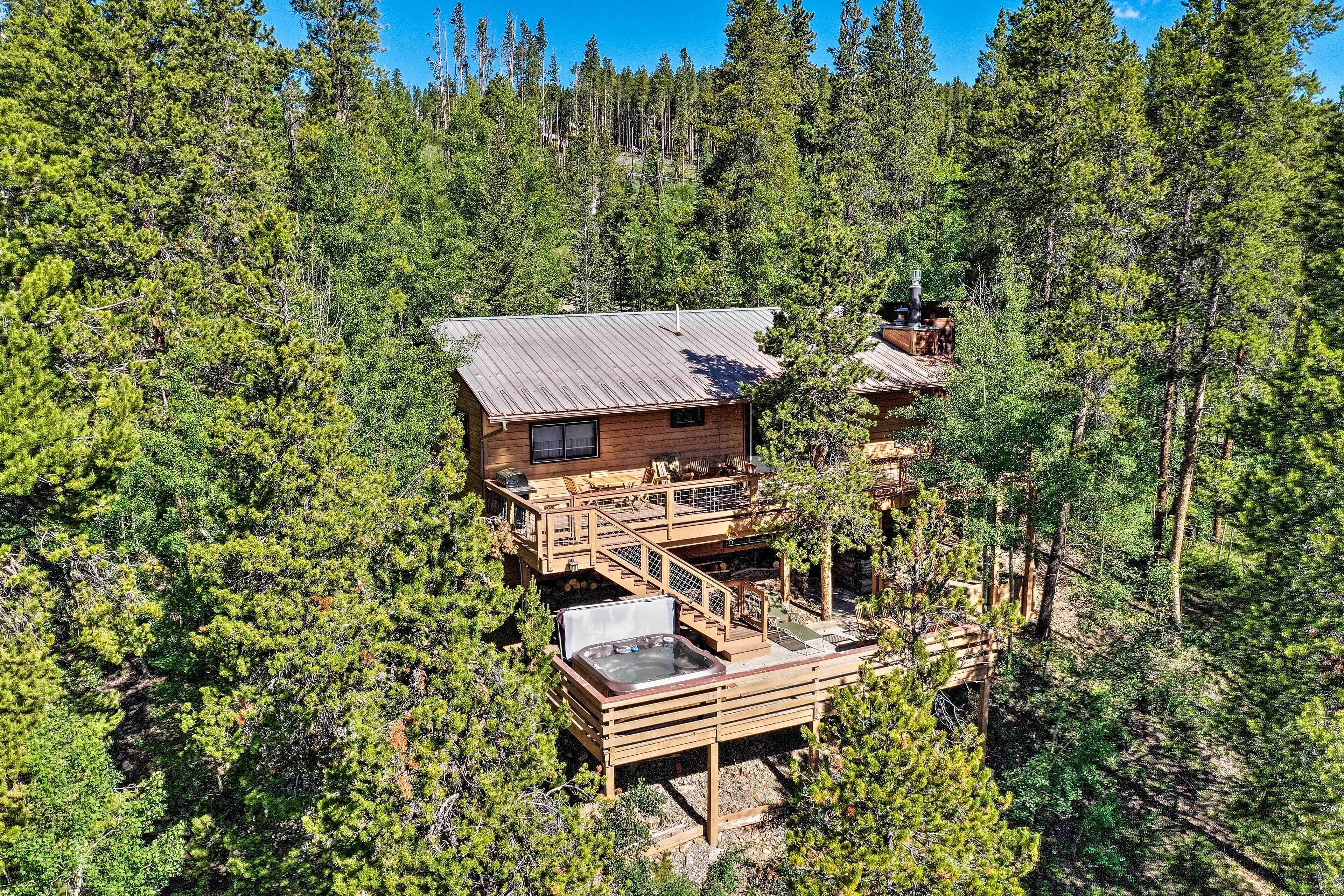 A wooden cabin with a hot tub, surrounded by dense forest.