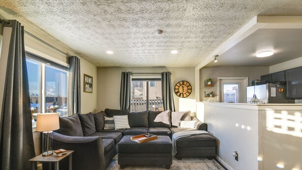 A living room with a sofa, ottoman, and a small table with a lamp. - Updated Townhome: Near Airport & Shopping! (Anchorage)