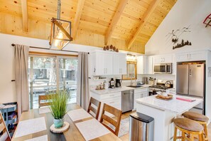 A modern kitchen with white cabinets, stainless steel appliances, and a wooden ceiling.