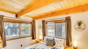 Ein Schlafzimmer mit einem Bett, zwei Nachttischen, einem Fenster mit Vorhängen und einem an der Wand befestigten Regal mit einer Pflanze.