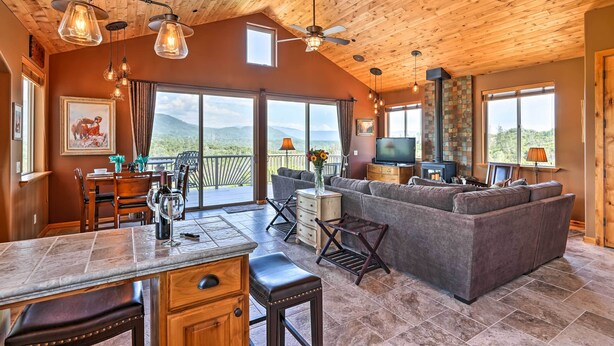 A spacious living area with a large gray sectional sofa, a wooden ceiling, and a view of mountains through large windows. - 28 Mi to Yosemite: Lovely Mtn Cottage w/ Deck! (North Fork)