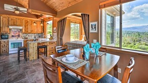 A spacious kitchen with wooden cabinets, a dining area with a table set for two, and a large window offering a scenic view. - 28 Mi to Yosemite: Lovely Mtn Cottage w/ Deck! (North Fork)