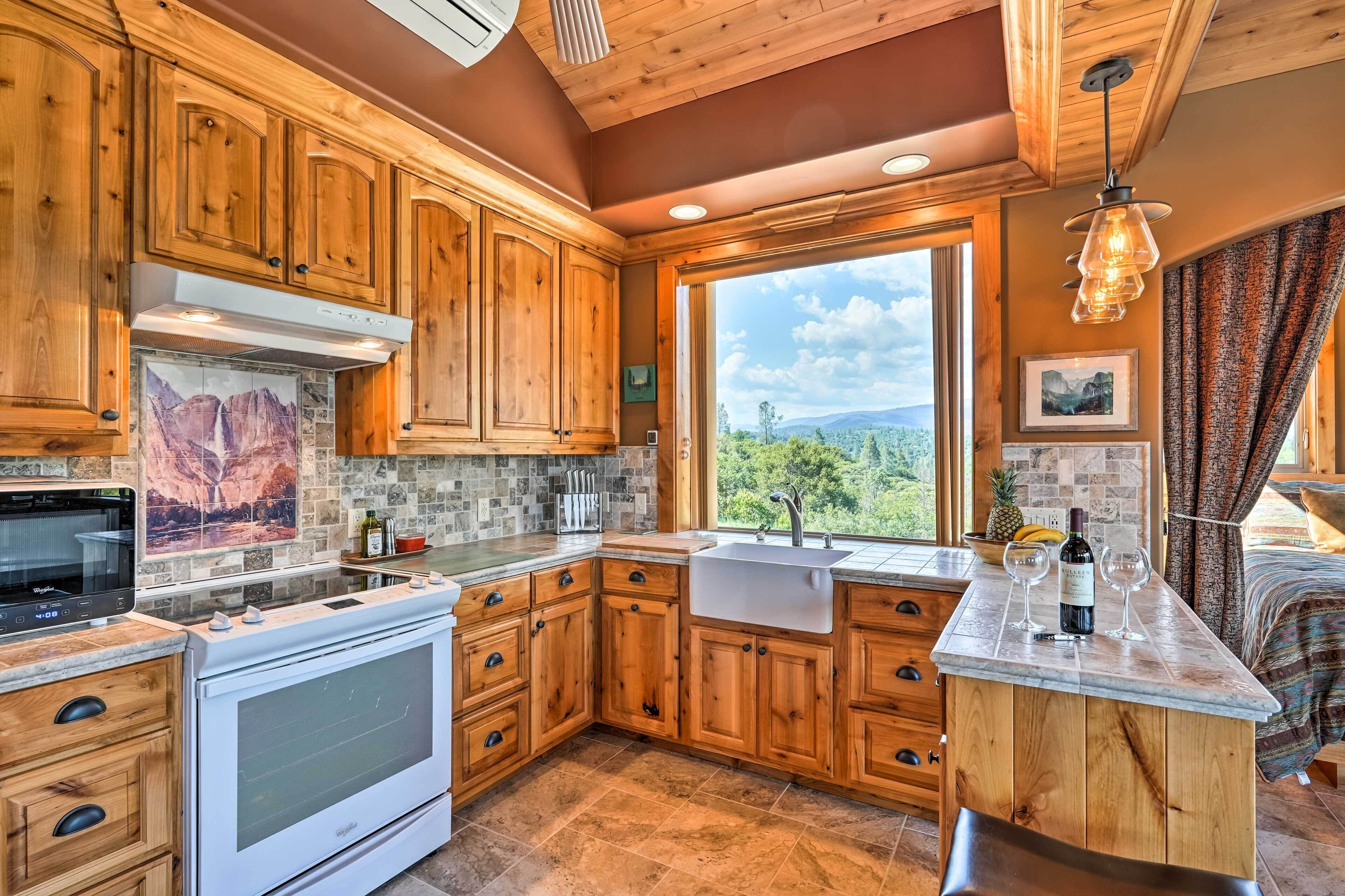 A kitchen with wooden cabinets, a built-in oven, a large window with a view of the outdoors, and a bar area with a wine bottle and glasses.