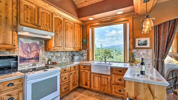 A kitchen with wooden cabinets, a built-in oven, a large window with a view of the outdoors, and a bar area with a wine bottle and glasses.