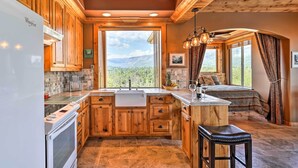 A modern kitchen with wooden cabinets, a central island, and a large window offering a mountain view. - 28 Mi to Yosemite: Lovely Mtn Cottage w/ Deck! (North Fork)