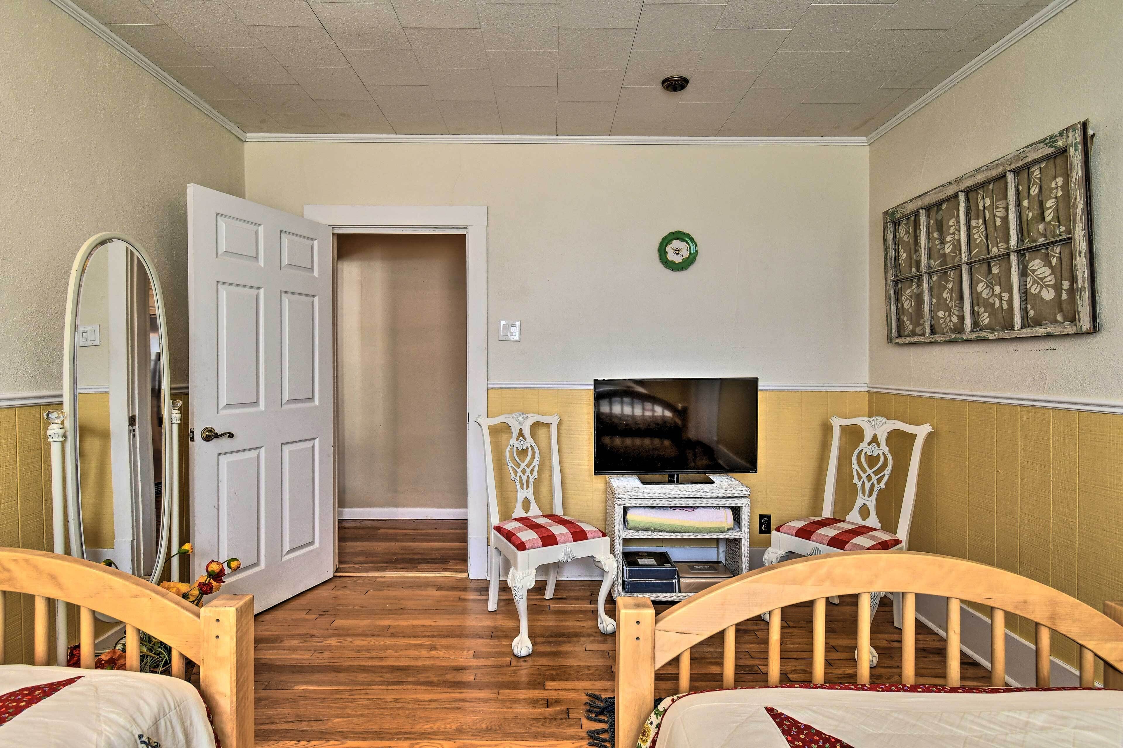 A bedroom with two wooden beds, a television, a white chair, and a mirror.