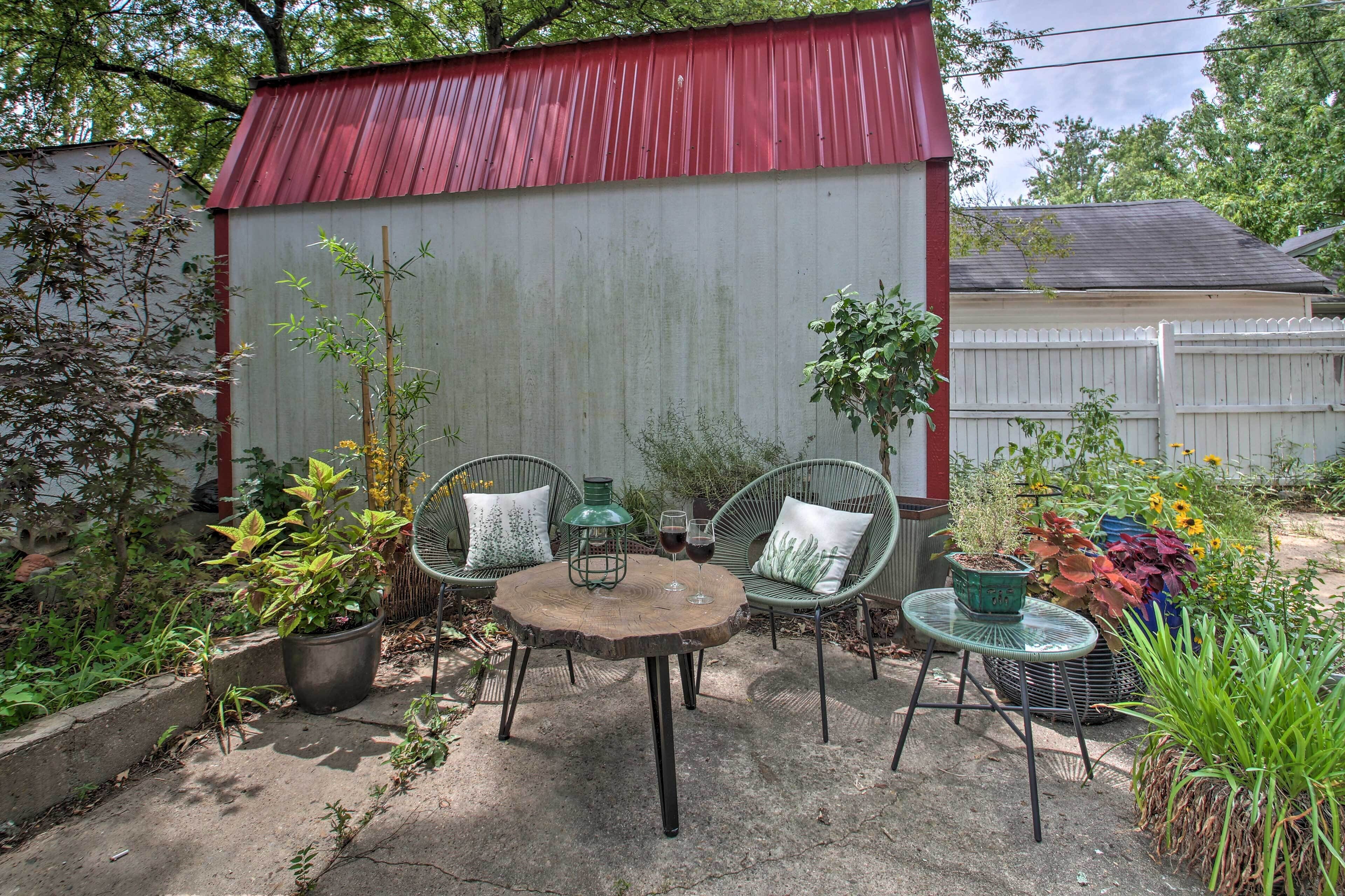 Un patio al aire libre con una mesa redonda, dos sillas de mimbre y plantas en macetas.