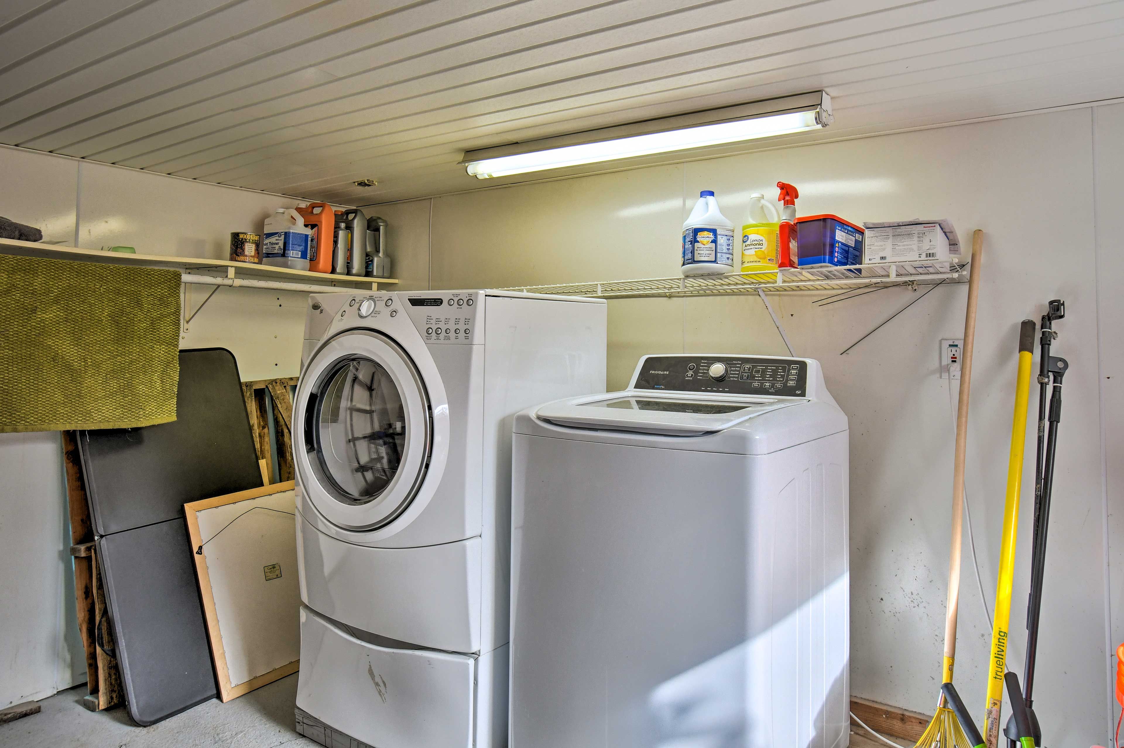 A laundry room with a washing machine, dryer, and shelving with cleaning supplies.