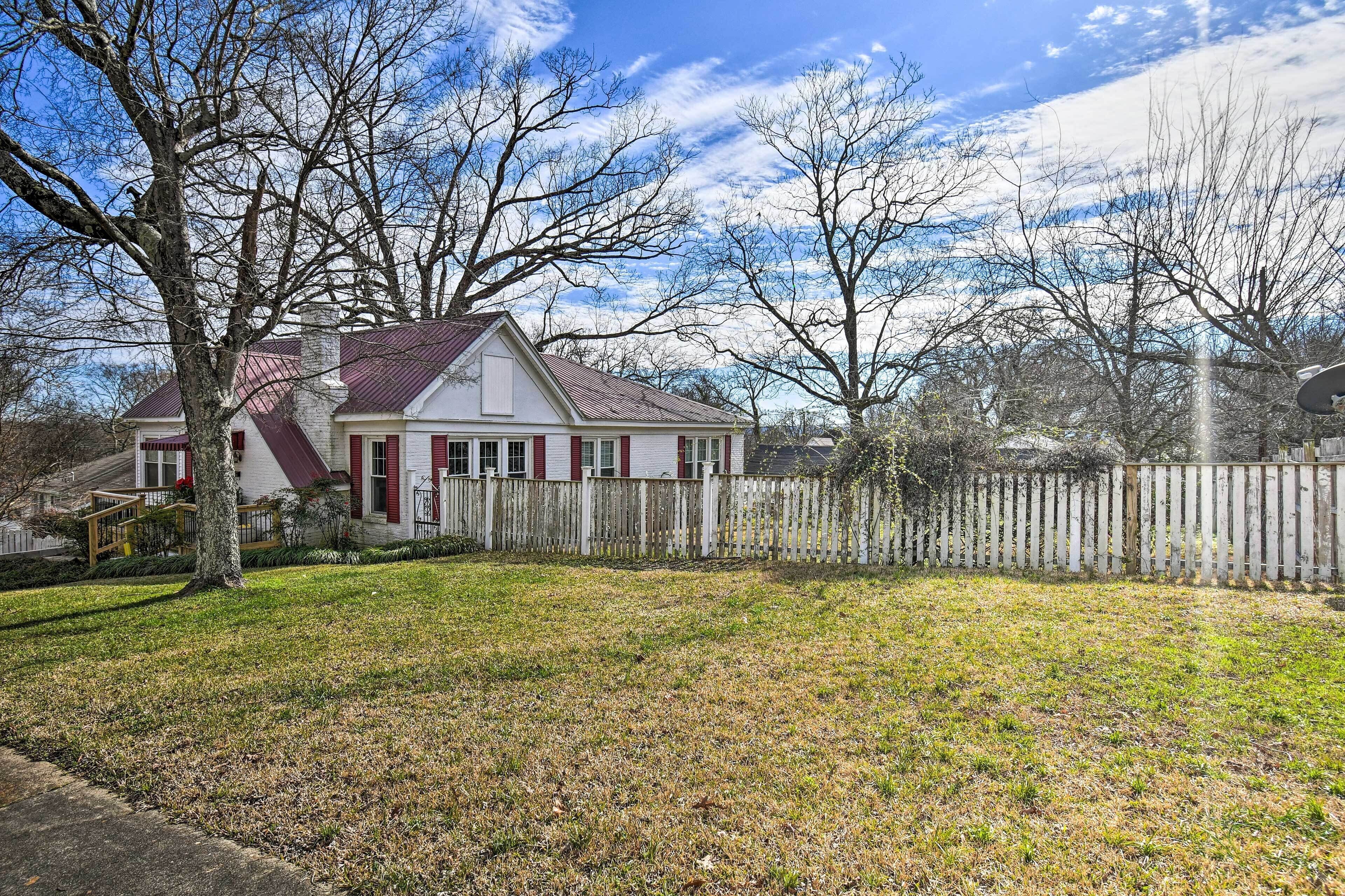 A single-story house with a red door and white trim, surrounded by a wooden fence and a grassy yard.