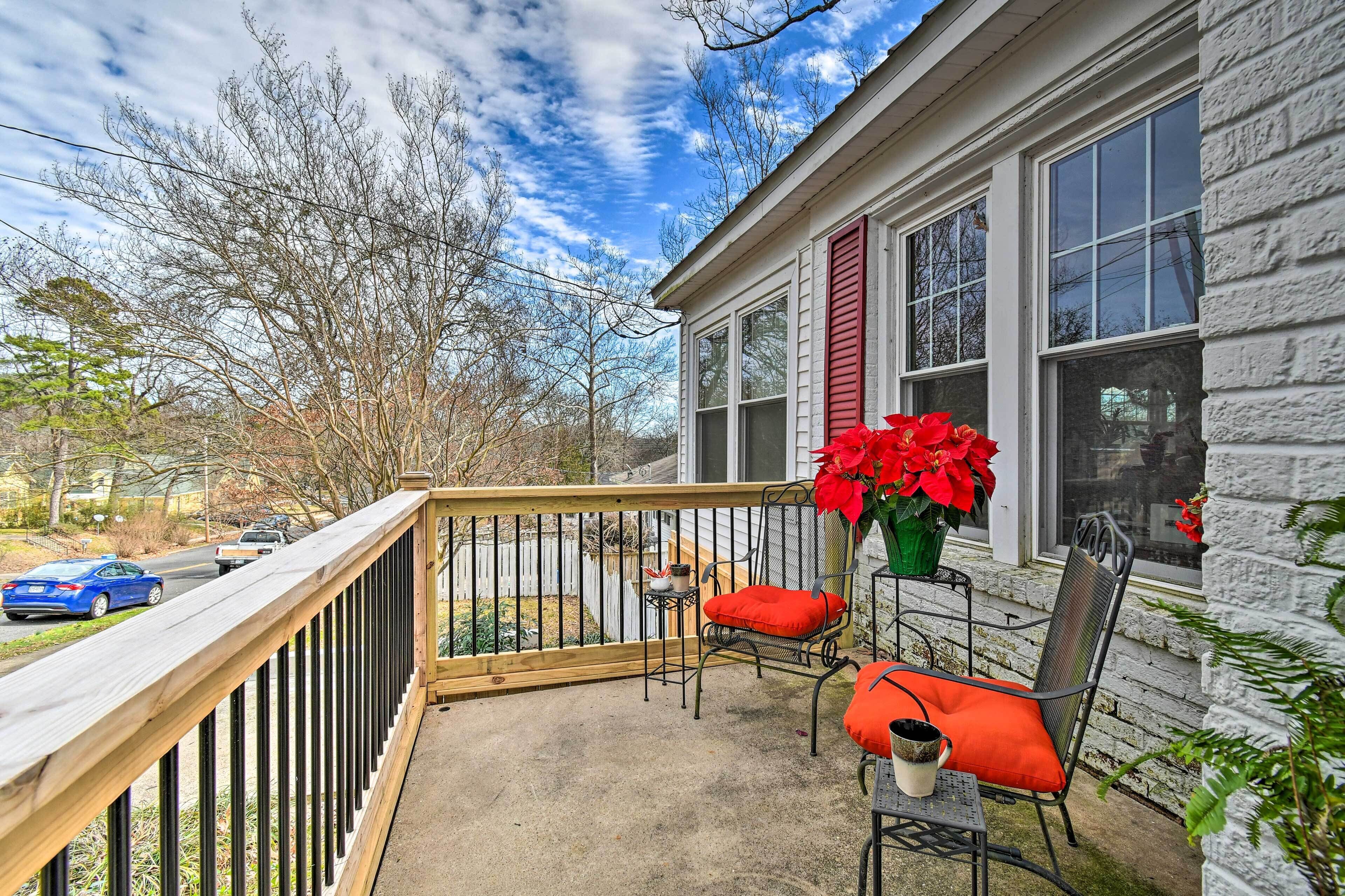 A covered porch with a wooden railing, a table, two chairs, and a potted plant with red flowers.