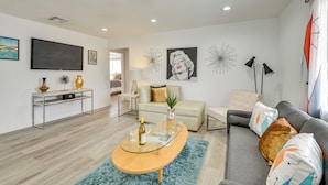 A modern living room with a glass coffee table, a sofa, a TV, and decorative wall art. - Pool & Mountain Views: Palm Springs Home (Palm Springs)
