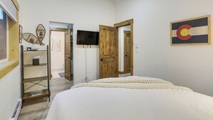 A bedroom with a bed, a wooden door, a TV, and a shelf. - Cozy Avon Condo w/ Grill: Walk to Ski Shuttle (Avon)