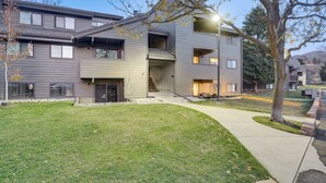 A modern multi-story residential building with a well-maintained lawn, a curved pathway, and a staircase leading to the entrance. - Cozy Avon Condo w/ Grill: Walk to Ski Shuttle (Avon)
