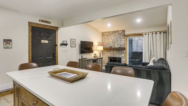 A modern kitchen with a stone backsplash, a dining area with a marble table, and a cozy seating area with a fireplace. - Cozy Avon Condo w/ Grill: Walk to Ski Shuttle (Avon)