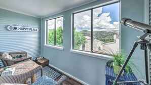 A cozy room with wicker furniture, a telescope, and a view of greenery and buildings. - Ruidoso Downs Condo w/ Mtn View + Balcony! (Ruidoso Downs)