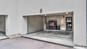 A parking garage with a concrete floor, a metal trash bin, and a door with an American flag. - Ruidoso Downs Condo w/ Mtn View + Balcony! (Ruidoso Downs)
