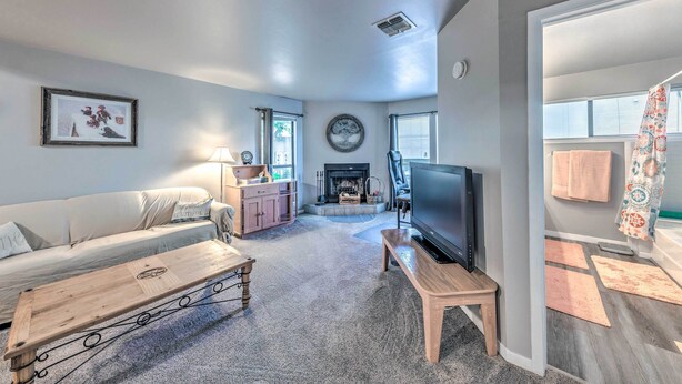 A living room with a sofa, coffee table, TV, fireplace, and a view of the outside. - Ruidoso Downs Condo w/ Mtn View + Balcony! (Ruidoso Downs)