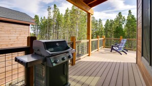 Une terrasse couverte avec un barbecue, une rambarde en bois et une chaise.