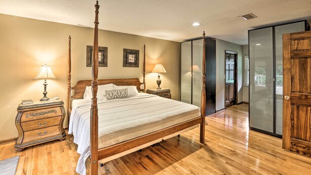 A four-poster bed with a wooden headboard, two bedside tables with lamps, a wooden nightstand, and a large mirror.
