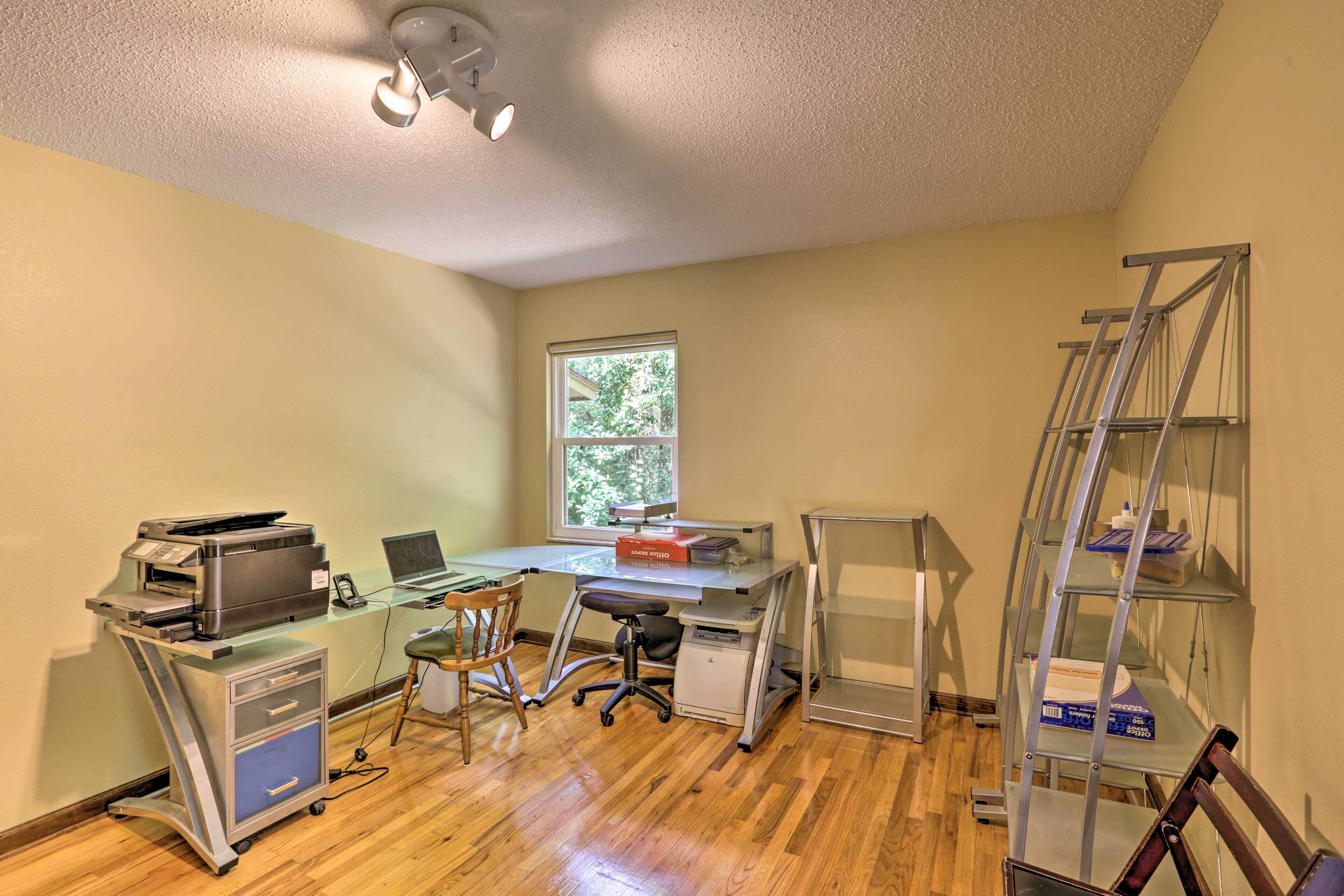 A small office with a desk, chair, printer, and shelves.