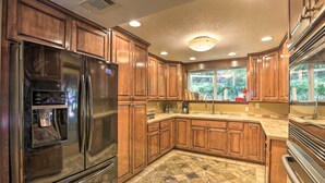 A kitchen with wooden cabinets, a stainless steel refrigerator, a built-in oven, and a window with a view of greenery.