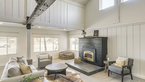 A spacious living room with a high ceiling, a fireplace, a sofa set, a coffee table, and a patterned ottoman. - Centrally Located Pinedale Vacation Rental! (Pinedale)